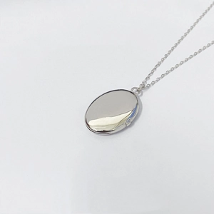 Dettaglio del ciondolo a medaglione ovale in argento lucido su sfondo bianco minimal
