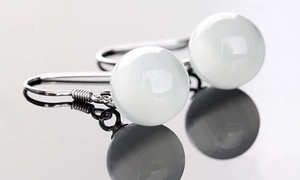 Macro shot of silver drop earrings featuring white round cat's eye stones on grey reflective base