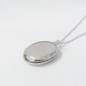 Macro detail of silver oval locket pendant showing the side opening hinge and smooth finish