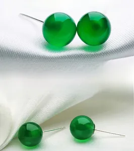 Detailed view of translucent green agate stud earrings on white silk fabric background