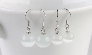 Macro detail of S925 silver cat's eye stone earrings hanging on a white ceramic bowl