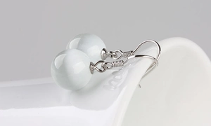 Macro shot of silver cat eye stone earrings hanging on a white ceramic edge