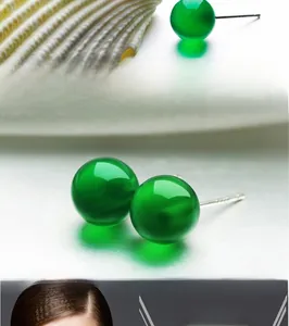 Detail of green chalcedony stud earrings with silver pins on a white shell background