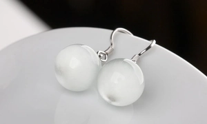 Macro shot of silver drop earrings featuring white cat-eye stones on a ceramic surface