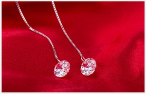 Macro detail of cubic zirconia drop earrings with silver box chain on red silk