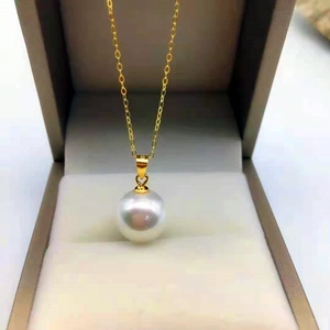 Detail view of a large white round pearl pendant on a gold chain in a velvet jewelry box