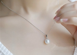 Detail of a minimalist round white pearl pendant necklace on a sleek silver chain