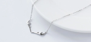 Macro detail of elegant S925 sterling silver deer antler pendant necklace on white ceramic