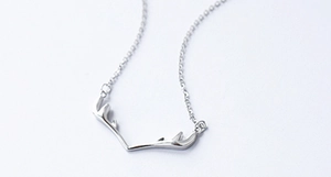Macro shot of minimalist silver reindeer antler pendant on a polished S925 chain necklace