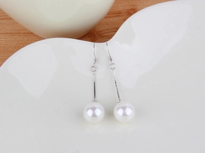 Close-up of elegant long dangle pearl earrings with silver hook on a ceramic dish