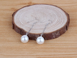 Close-up of S925 sterling silver hook and white pearl on natural wood base