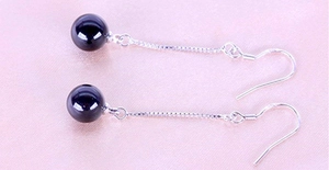Close-up of long tassel silver earrings with black onyx beads on purple silk fabric