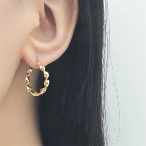 Close-up of a model wearing golden spiral twisted hoop earrings with floral design