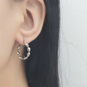 Detail view of a twisted sterling silver hoop earring worn by a model in a minimalist style