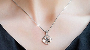 Detail view of a sparkling rotating four-leaf clover pendant on a model's neck