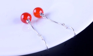 Macro shot of red agate beaded drop earrings with long silver tassels on a ceramic plate
