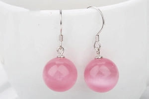 Detail of pink cat-eye stone drop earrings hanging on a white porcelain cup rim