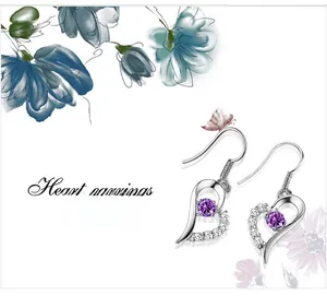 Detail of silver heart earrings with purple gemstone and pavé stones on white background