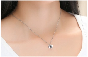 Détail du collier avec pendentif cube géométrique en argent S925 sur le cou d'un modèle
