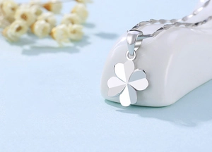 Macro view of a polished silver clover pendant with heart-shaped leaves on a ceramic stand