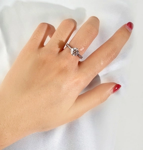 Detailed view of s925 silver six-prong moissanite ring worn on hand with silk background