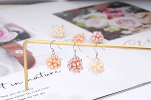 Detail of handmade pearl cluster earrings in pink and cream on a gold jewelry stand