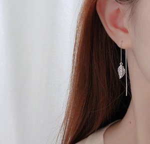 Macro detail of S925 silver leaf earrings featuring long tassel chains on a model