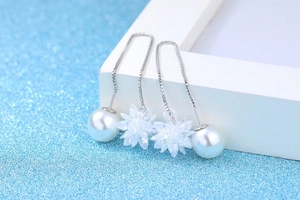 Macro detail of long silver threader earrings with white pearls and zircon flowers