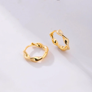 Macro shot of gold-tone Moebius hoop earrings featuring twisted texture and glossy finish