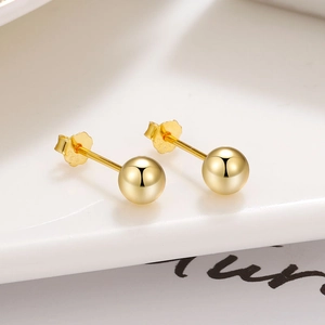 Boucles d'oreilles boules en argent S925 doré poli sur un plateau en céramique blanche