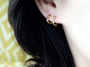 Close-up of a woman wearing the gold Mobius twisted hoop earrings with a wavy design