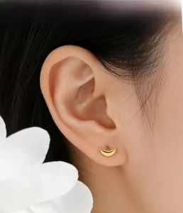 Close-up of polished gold crescent moon stud earrings worn by a model with floral accents
