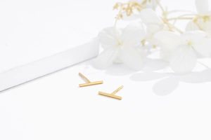 Macro shot of minimalist S925 sterling silver gold-plated T-bar stud earrings on white stone