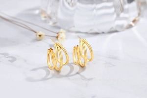 Detail view of triple-row gold hoop earrings on a luxury white marble background