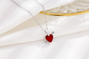 Dettaglio ravvicinato del ciondolo a cuore rosso con freccia d'argento su raso bianco