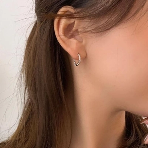 Gros plan de boucles d'oreilles créoles torsadées en argent montrant la texture sur le modèle