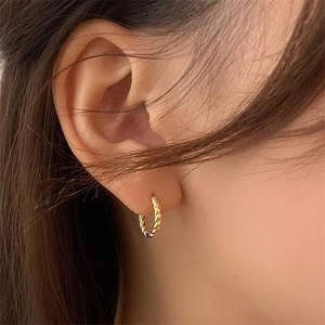 Gros plan de boucles d'oreilles créoles torsadées dorées portées au style rétro épuré