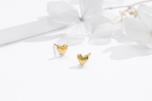 Close-up of minimalist heart stud earrings in golden finish on a white floral background