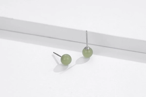 Detail of green stone stud earrings on white geometric steps with silver needles
