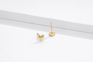 Close-up of golden S925 sterling silver heart stud earrings on a white geometric stand