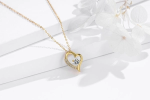 Detail shot of a golden heart pendant necklace with shimmering crystals on a white pedestal