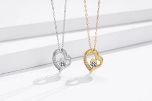 Macro detail of silver and gold heart pendants with floating center stones on a white stand