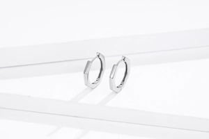 Close-up of minimalist S925 sterling silver hexagonal hoop earrings on a white podium