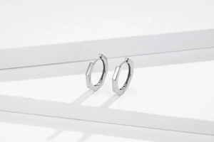 Macro shot of polished S925 sterling silver hexagonal huggie earrings on white platform