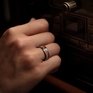 Men's black titanium ring with inlaid acacia wood grain shown on a hand