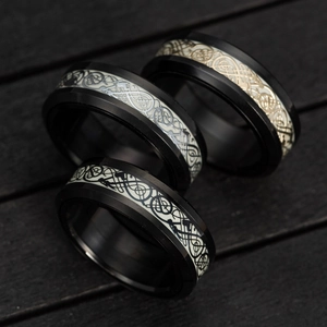 Macro detail of men's black spinning rings with intricate luminous dragon pattern inlay