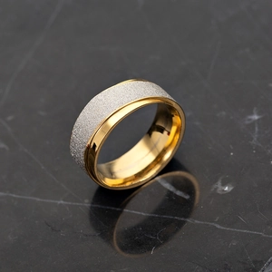 Détail macro d'une bague bicolore en acier avec centre sablé argent et bords dorés polis