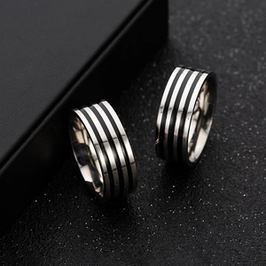 Detail shot of two 8mm stainless steel rings with black enamel stripes on a textured surface