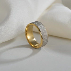 Détail d'une bague en acier doré avec une finition argentée givrée et mate sur la surface