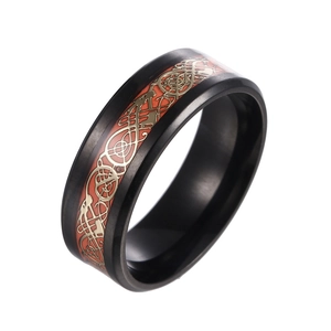 Detailed close-up of black brushed steel ring with gold Celtic dragon inlay on orange base